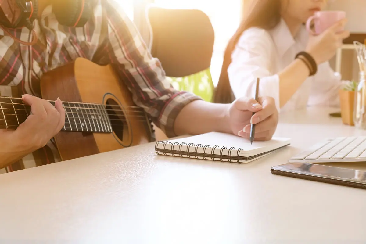 Person writing notes while playing guitar.