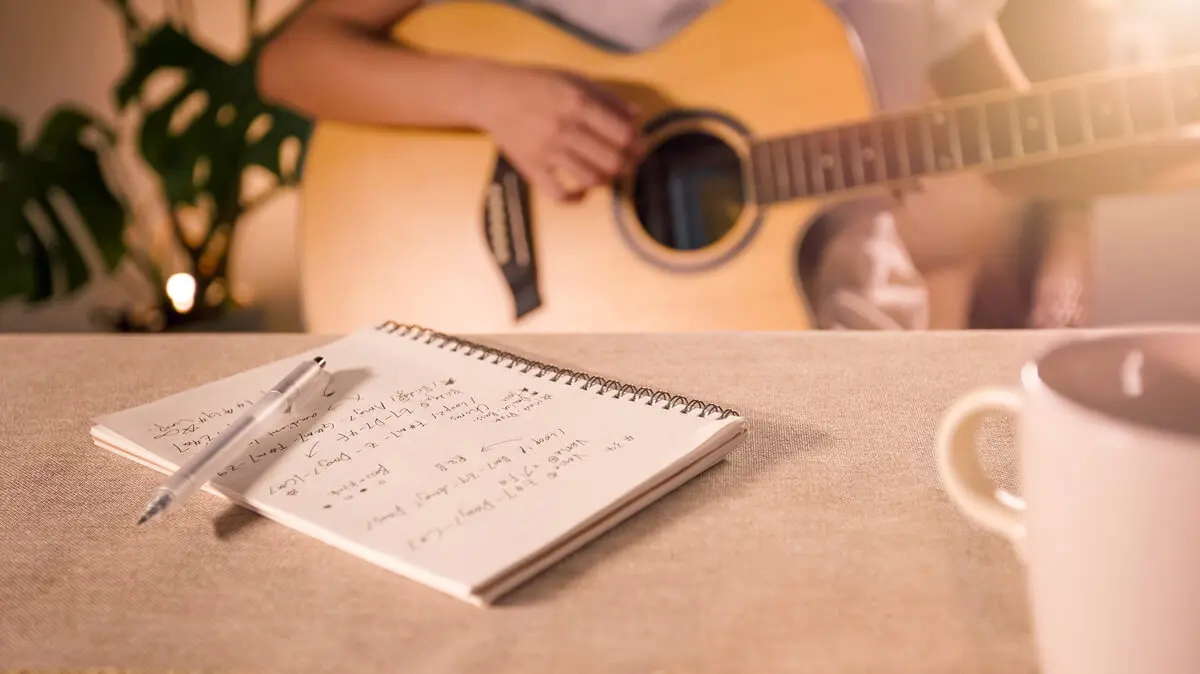 Guitar playing with notebook and coffee cup.