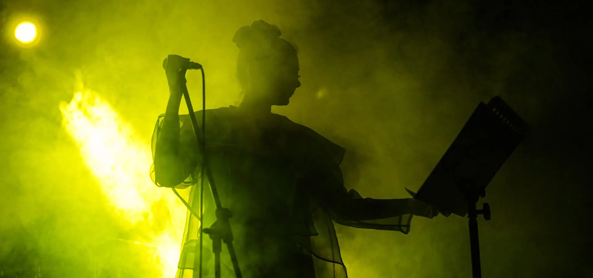 Singer performing on stage with yellow lighting.